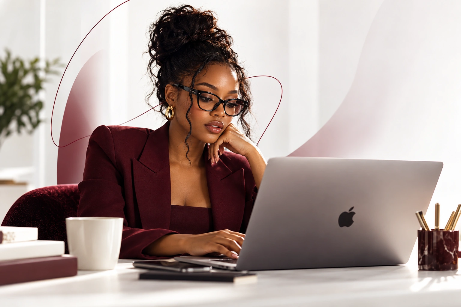 Woman in a burgundy blazer working on a laptop in a bright workspace